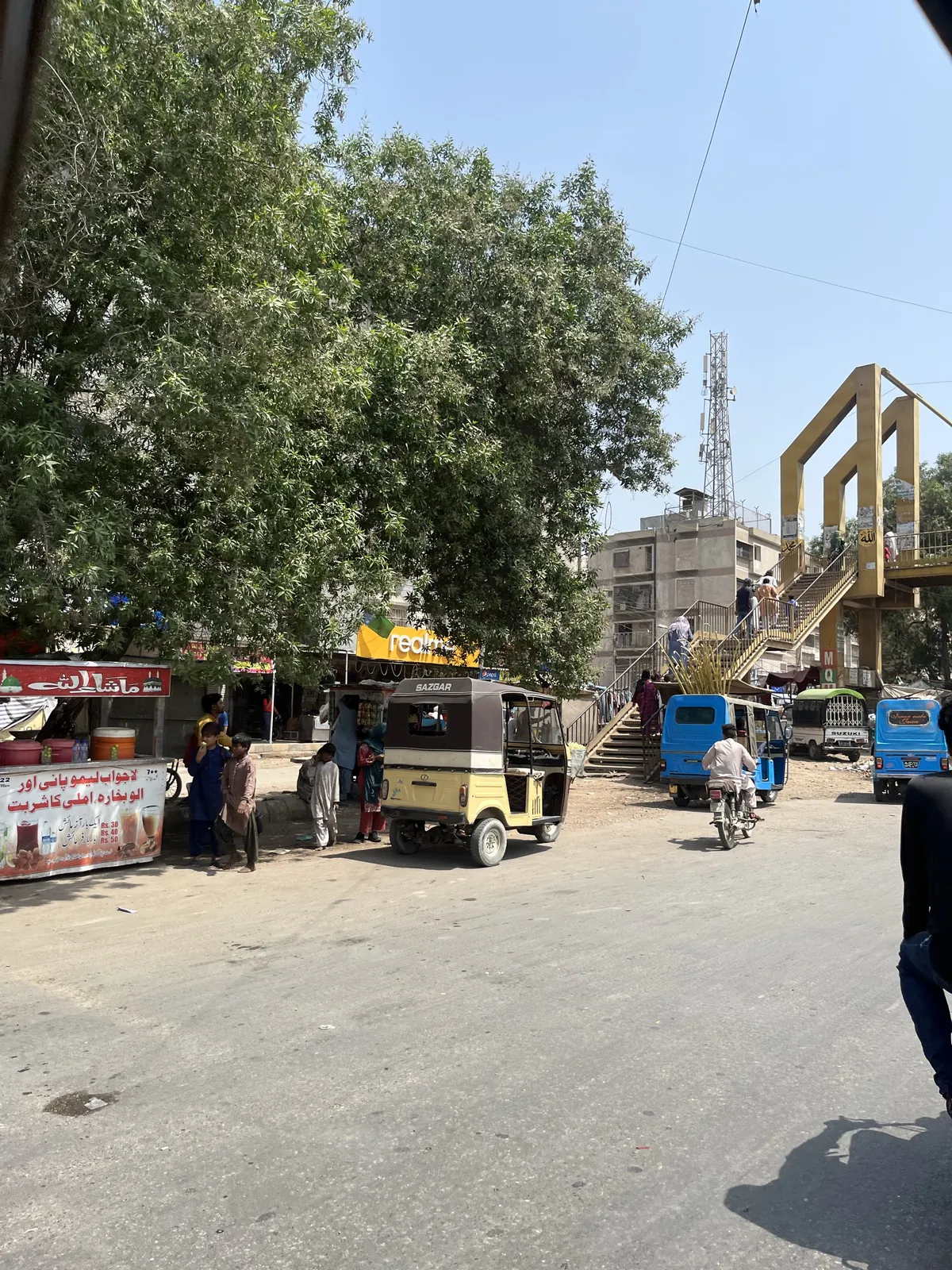 A Karachi street with rickshaws, roadside stalls and a pedestrian overpass.